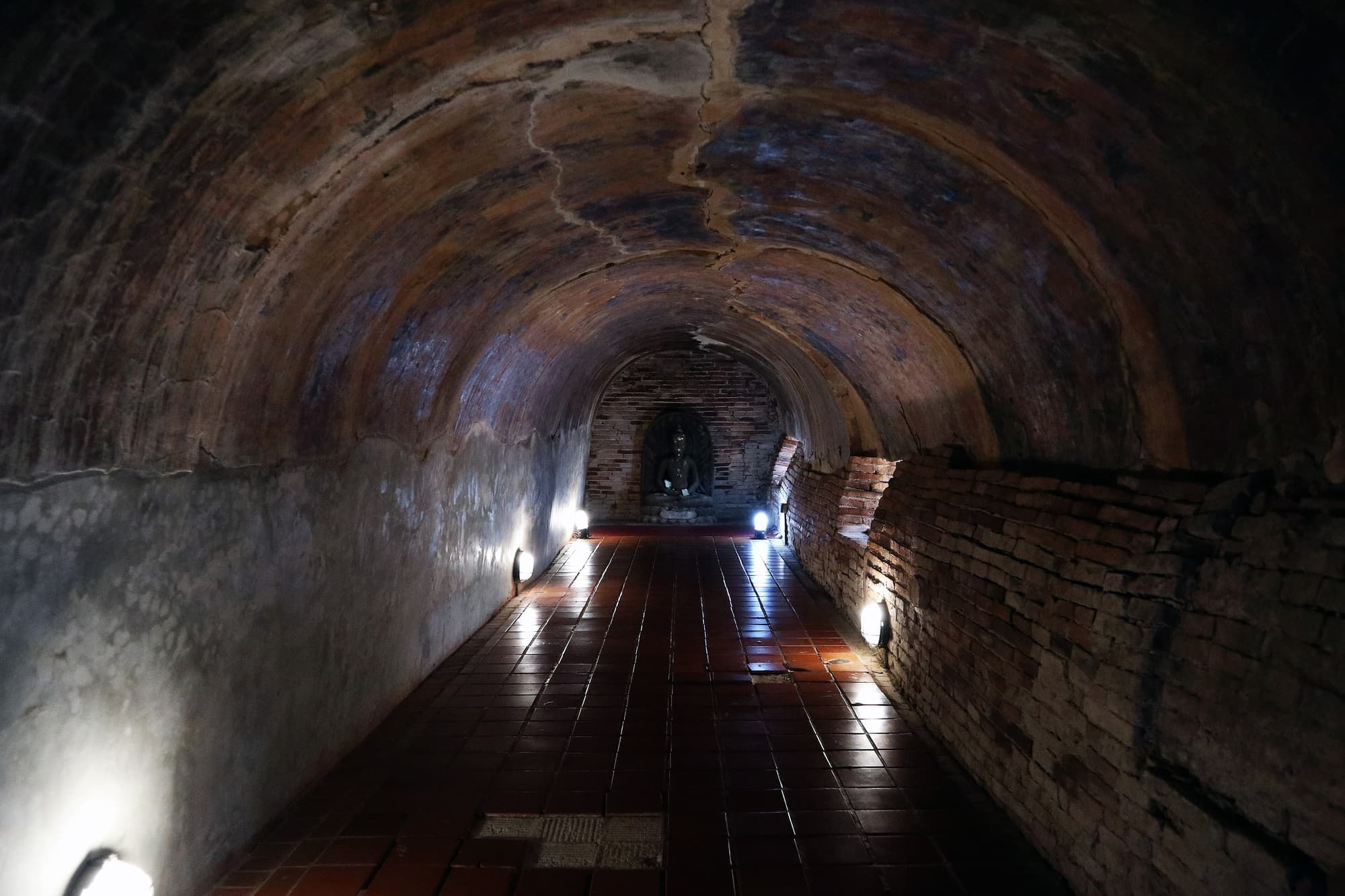 Lamp-lit brick tunnel with a Buddha image at the end, Wat Umong